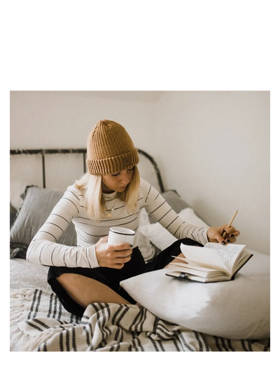 young woman with a cup of coffee while journaling in bed