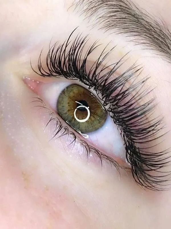 Close-up of a green eye with long, curled lashes and a groomed eyebrow.