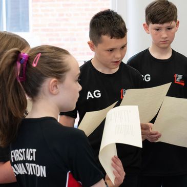 Students, standing in a group, looking at scripts in their acting class.