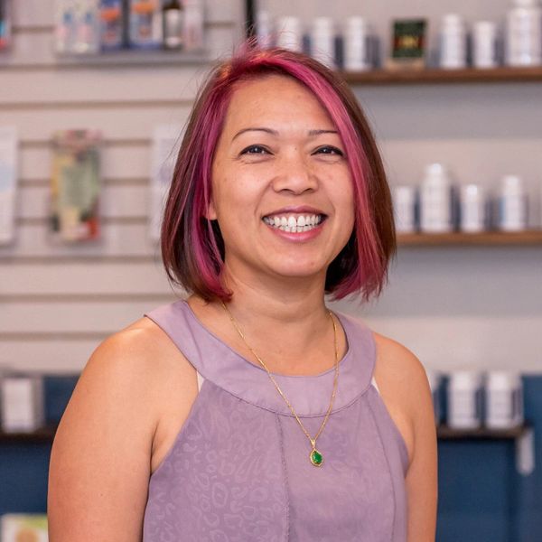 Smiling woman with pink hair and purple dress in a wellness store.