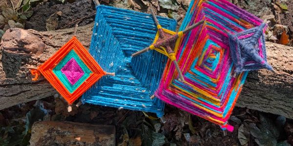 Colorful yarn crafts wrapped around sticks, displayed on a log outdoors.