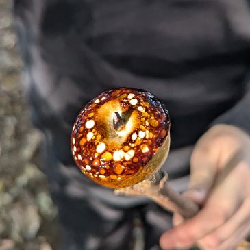 A toasted marshmallow on a stick held by a person wearing dark clothing.