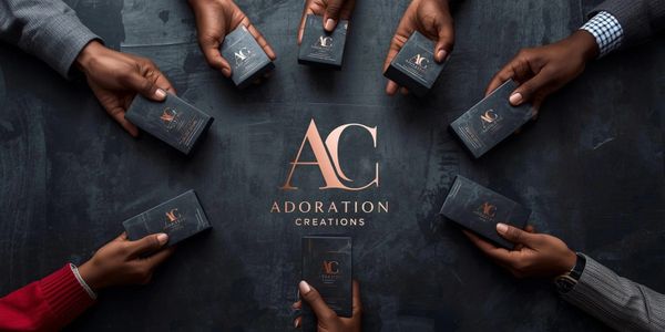 Hands holding Adoration Creations boxes around the logo on a dark surface.
