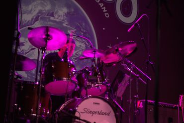 Drummer playing on a Slingerland drum set under purple stage lights.