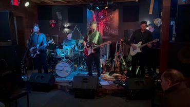 A band performs live on a dimly lit stage with colorful lights.