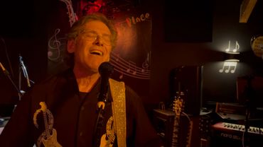 An older man passionately singing and playing guitar on stage in a dimly lit venue.