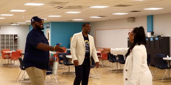 Three people greeting each other in a room with chairs and tables.