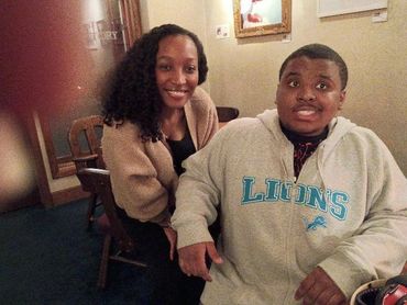 A smiling woman and a man in a Lions sweatshirt sitting indoors.