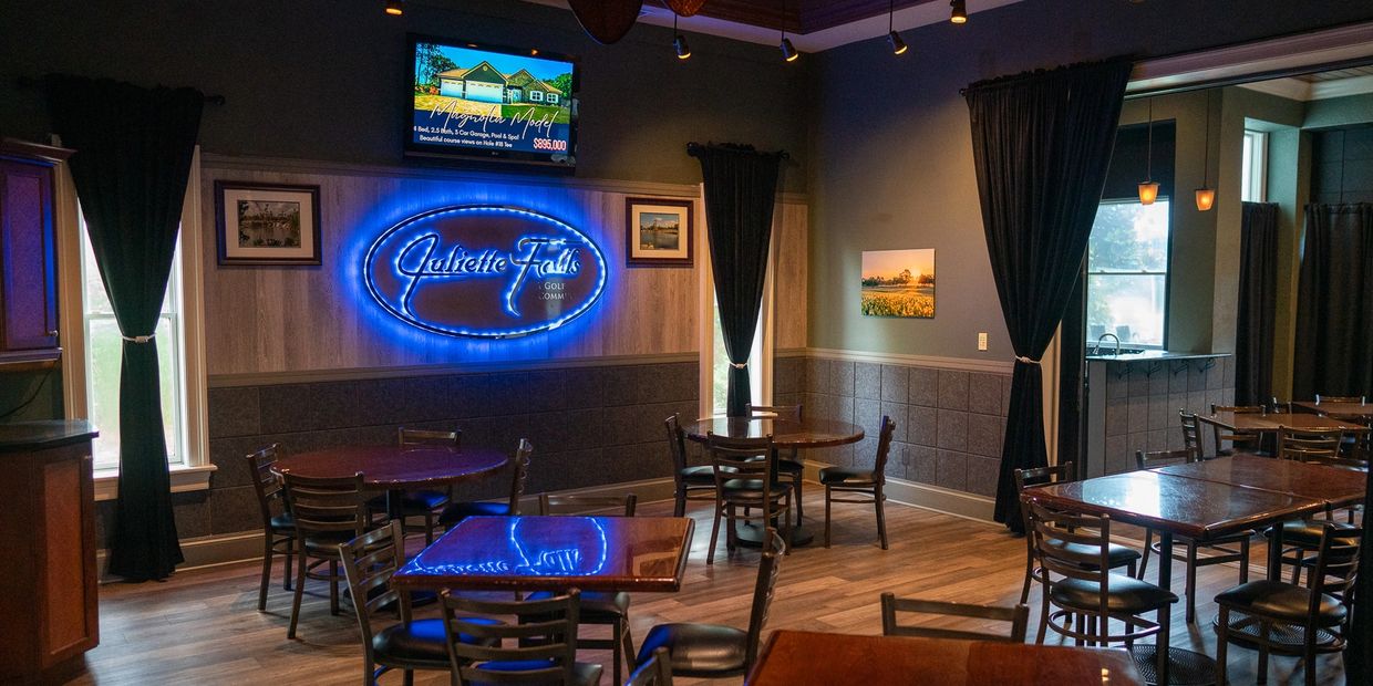 Cozy dining area with wooden tables, chairs, and blue neon Juliette Falls sign.
