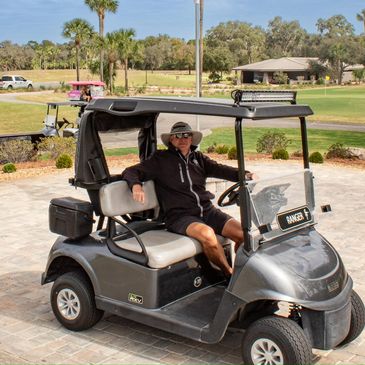 Man sitting in a golf cart on a sunny day at a golf course.