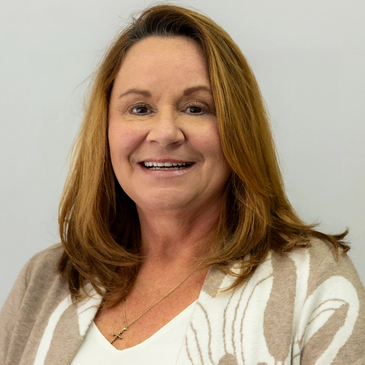 Smiling woman with brown hair wearing a beige patterned cardigan.