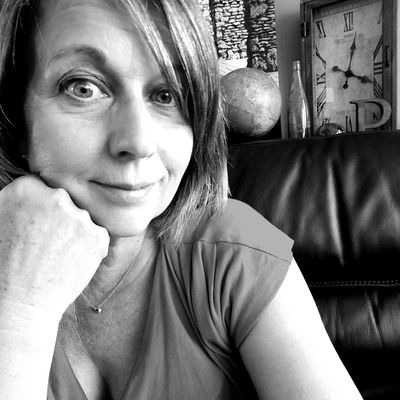 Black and white photo of a woman smiling with a vintage clock in the background.