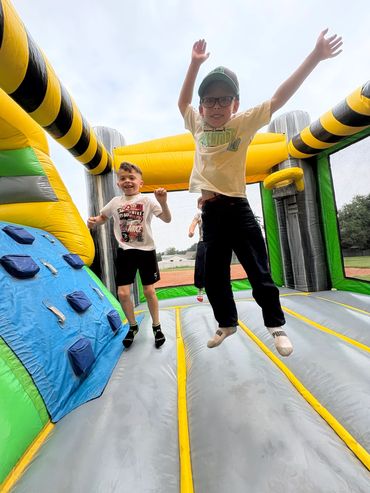 Two kids jumping on an inflatable bounce house outdoors.