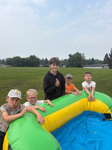 Five boys with inflatable pool outdoors on green grass.