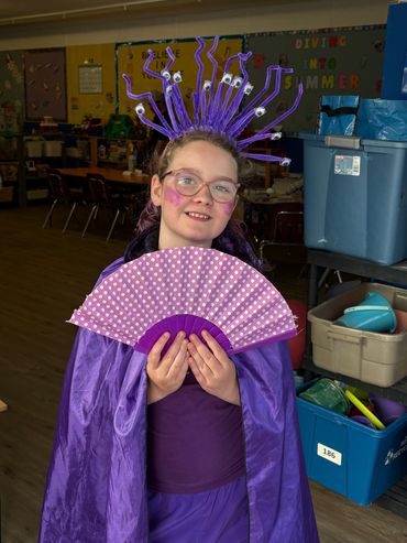 Girl in purple costume holding a pink polka dot fan.