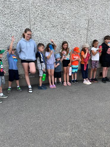 Group of children standing in a line outdoors against a wall.