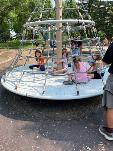 Children playing on a round rope climbing structure at a park.