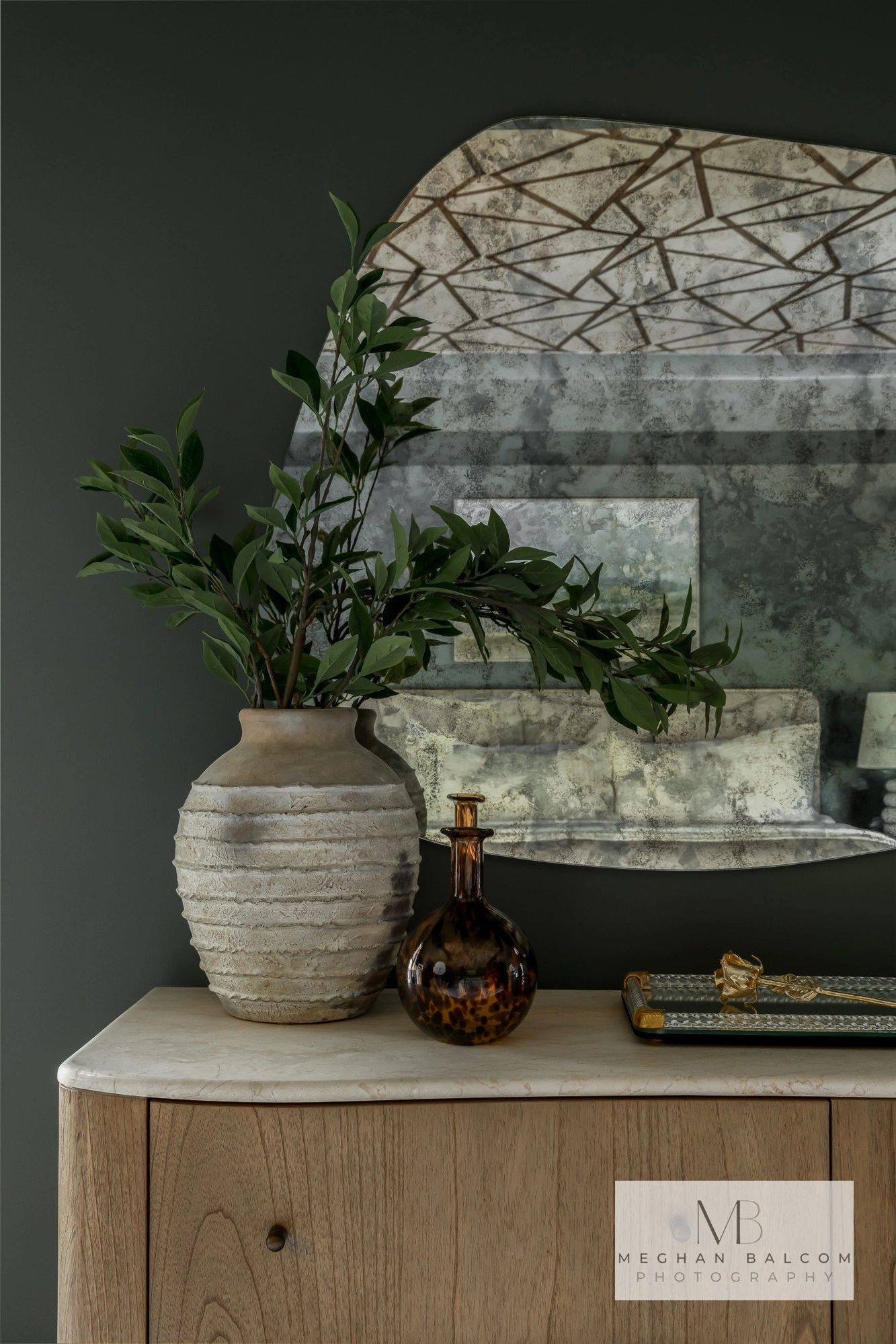 Rustic vase with green plant and antique mirror reflection.