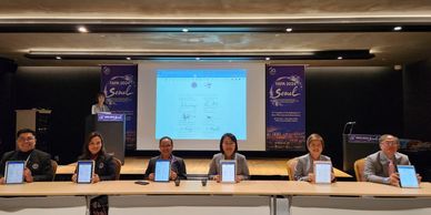 Six individuals seated at a table displaying tablets during a conference in Seoul.
