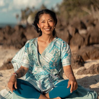 Woman smiling while sitting cross-legged on the beach.
