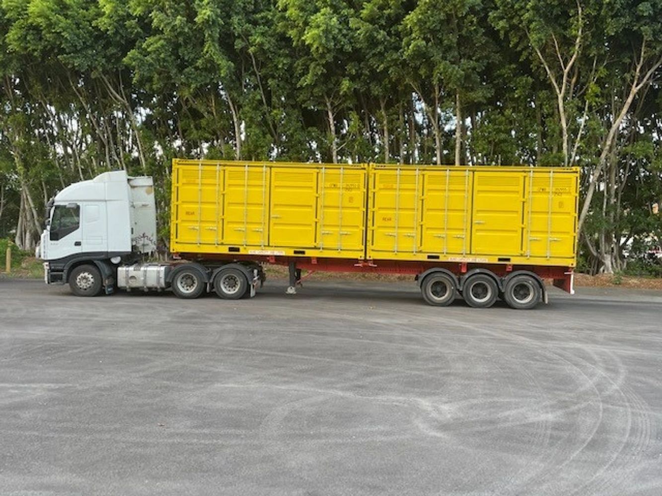 White truck with bright yellow cargo container parked on asphalt near trees.