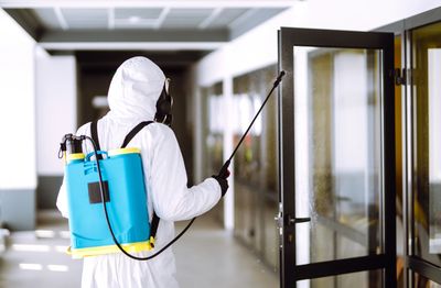 cleaner wearing PPE disinfecting business with COVID-19 coronavirus spray mist fogger service