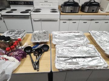Kitchen table with foil-covered trays and cooking utensils ready for food preparation.