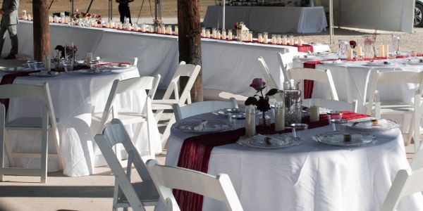 Elegant outdoor event setup with white chairs and tables, decorated with red accents and candles.