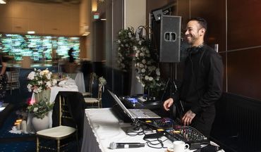 DJ smiling while working at a laptop and mixer in an event venue.