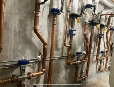 Copper plumbing pipes with blue valve handles installed on a concrete wall.