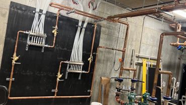 Industrial pipes and valves in a mechanical room.