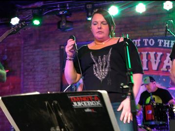 Woman singing on stage with band in a dimly lit venue.