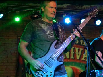 Man playing electric bass guitar on stage under colorful lights.