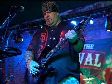 Musician playing electric guitar on stage in a dimly lit venue.