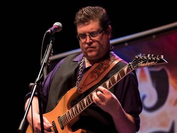 Man playing electric guitar on stage with microphone nearby.
