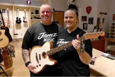 Two people holding a guitar in a music store.