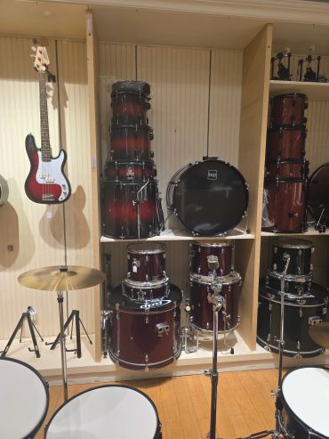 A music room with stacked drums and a bass guitar hanging on the wall.