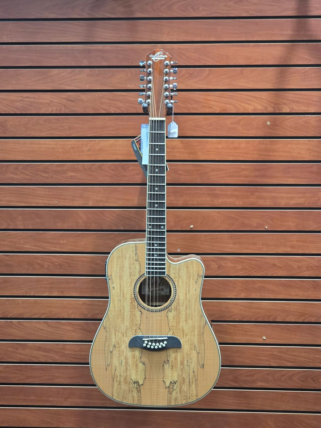 A 12-string acoustic guitar hanging on a wooden wall.