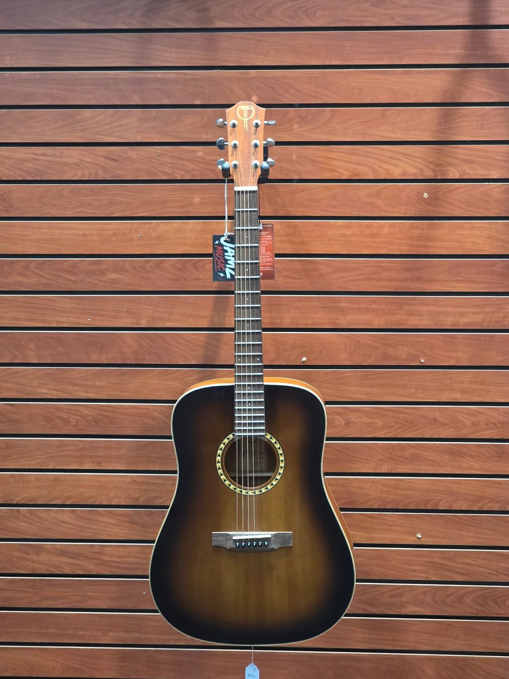 Brown acoustic guitar hanging on wooden wall.