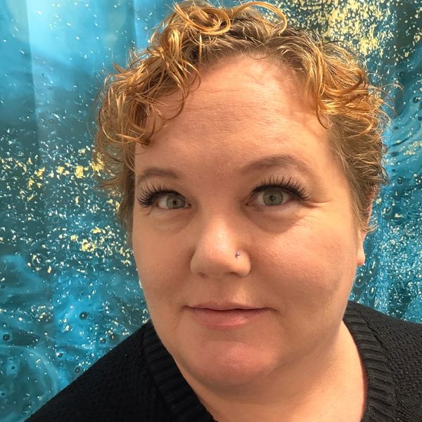 Close-up of a woman with curly hair and a nose piercing against a blue textured background.