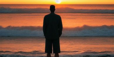 A man looking towards the ocean standing on a beach at sunset 