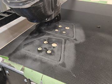 CNC machine carving holes into a carbon fiber sheet with dust and tape around.