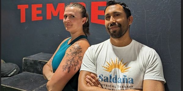 Two confident people standing back-to-back in a gym.