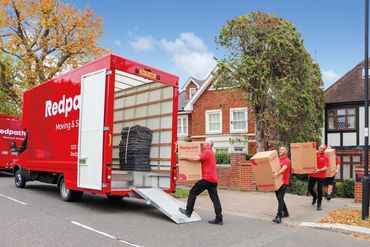 Moving crew unloading boxes from Redpack moving truck in a residential neighborhood.