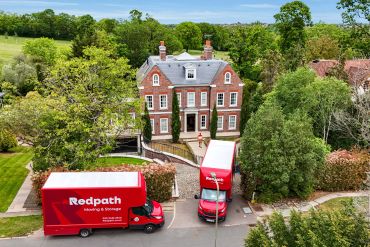 Redpath moving trucks outside a large brick house surrounded by greenery.