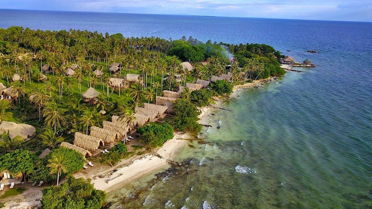 Isla tropical con cabañas y playa frente al mar.