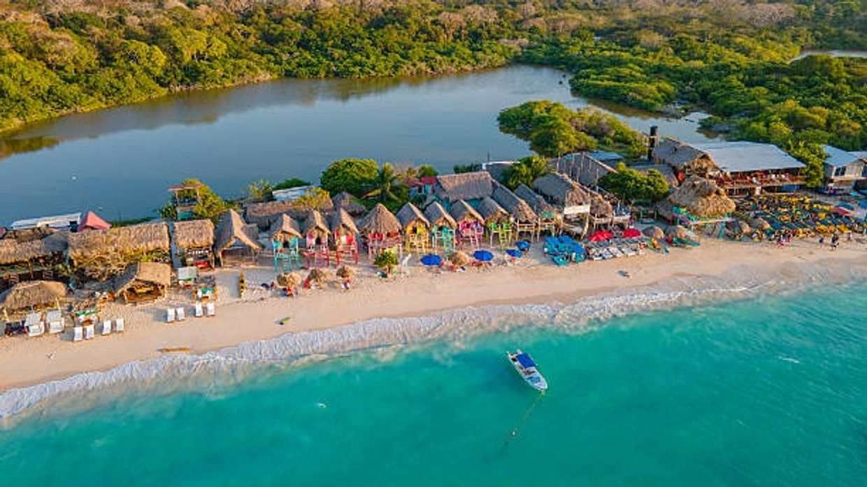 Vista aérea de una playa con cabañas y aguas turquesas.
