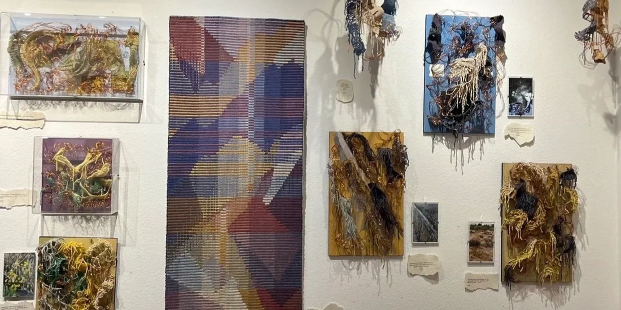 Mixed media art pieces with yarn and thread on canvases displayed on a white wall.
