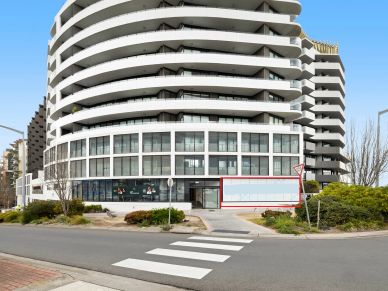 Modern curved building with empty storefront space.