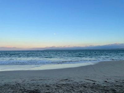 Calm ocean waves gently meet the sandy shore under a clear blue sky.